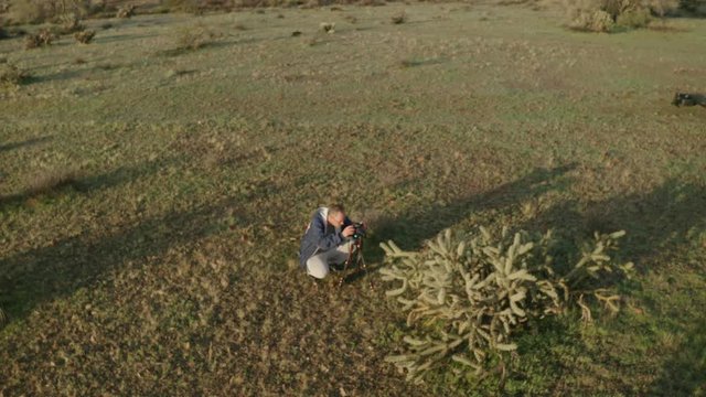 A drone flying circles around a photographer sitting low to the ground capturing images of a staghorn cactus in the Sonoran Desert of Arizona.