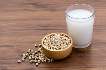 Closeup white Job's tears ( Adlay millet or pearl millet ) in wooden bowl and glass of fresh millet milk isolated on wood table background. 