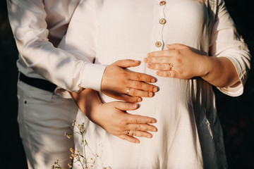 Plump pregnant caucasian lady dressed in a white dress being embraced by her lover are posing against the sunshine