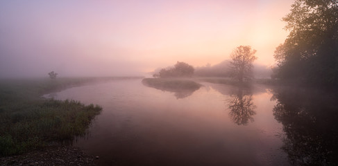 Fototapeta na wymiar Calm River with a Pink Sunrise with Fog and Mist with Trees and Reflections