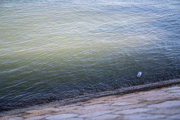 Single plastic water bottle litter washing up on sea bank causing pollution