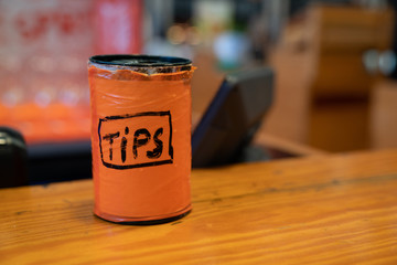 Orange tips jar sitting on bar countertop for bartender and drinks - Powered by Adobe