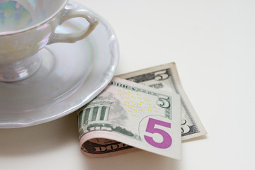 five dollar bill under the cup on white table. Tip for the waiter