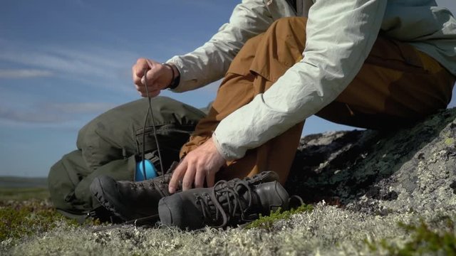 A hiker lacing his shoes sitting on the grass in tundra.