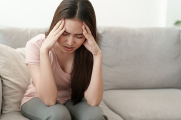 Asian woman are holding their hands to the head in pain while sitting on the sofa at home, Young women have severe headaches from migraines, Health and illness concept