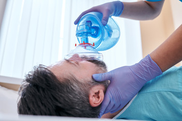 Close-up of unrecognizable doctor in surgical glove giving oxygen to patient while trying to save...