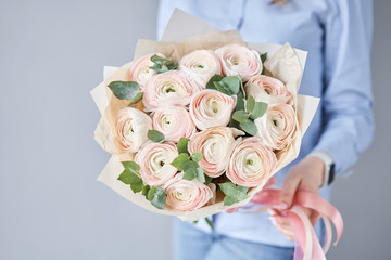 Persian buttercup in womans hands. Bunch pale pink ranunculus flowers with green eucalyptus. The work of the florist at a flower shop