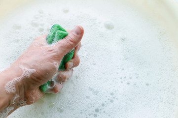 Household sponge in hand on the background of soap suds. The concept of a household.