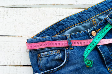 Top of denim trousers, on a wooden background. Blue jeans with a measuring tape instead of a belt. jeans with a measuring tape around the waist. The concept of a healthy lifestyle and diet.