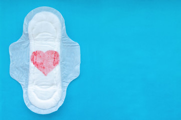 Women's pad with a red heart on a blue background. The concept of the menstrual cycle.
