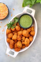 Moong dal ke pakode, ram laddoo, bhajias, Moongode or fritters. served with green mint and coriander chutney. Served over light background. Selective focus. with copy space.
