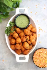 Moong dal ke pakode, ram laddoo, bhajias, Moongode or fritters. served with green mint and coriander chutney. Served over light background. Selective focus. with copy space.
