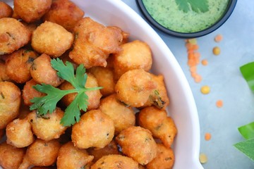 Moong dal ke pakode, ram laddoo, bhajias, Moongode or fritters. served with green mint and coriander chutney. Served over light background. Selective focus. with copy space.