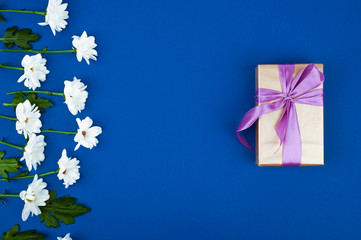 Gift box and flowers on blue table. Greeting card for Birthday, Womans or Mothers Day. Top view