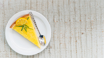 Slice of yellow lemon cake decorated with a slice of lemon, on a white plate on wood table background. Directly above view. Minimalist style. Delicious fruit dessert.food concept background with space