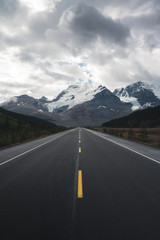Naklejka premium Beautiful Canadian Rockies Landscape with Mountains and symmetrical road during Cloudy Summer Weather 