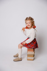 child girl in school uniform sitting on a stack of books isolated on a white background