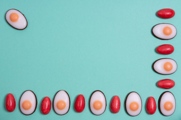 Little red Easter eggs arranged alternately with Easter candies designed as egg white with yolk on an aqua menthe surface
