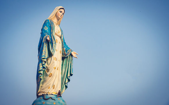 The blessed Virgin Mary statue figure. Catholic praying for our lady - The Virgin Mary. Blue sky copy space on background
