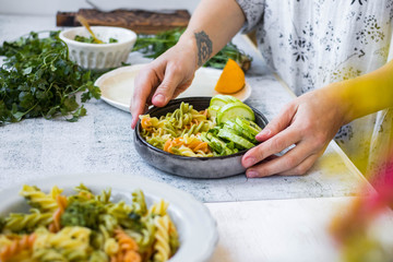 Woman serve vegan pasta on table, colorful macaroni with vegetables on plate. Mediterranean Italian traditional healthy food on lunch or vegetarian dinner.