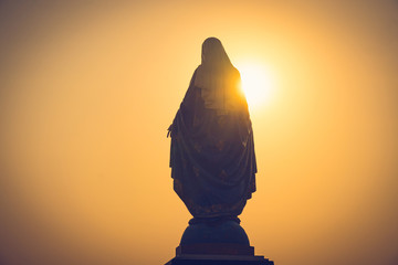 Silhouettes of the blessed Virgin Mary statue figure in a warm tone - sunset scene. Catholic praying for our lady - The Virgin Mary.