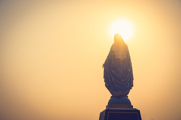 Silhouettes of the blessed Virgin Mary statue figure in a warm tone - sunset scene. Catholic praying for our lady - The Virgin Mary.