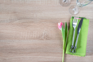 Table setting with pink tulip, forged fork and knife on green napkin, set of wineglasses on wooden...