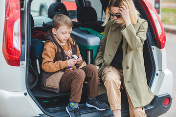 little kid sitting with mother in car trunk full of luggage eating chocolate candies