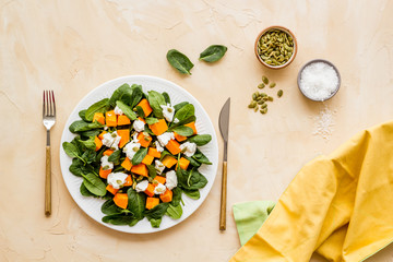 Light dish for lunch. Salad with pumpkin and basil on beige background top-down.