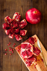 Fototapeta na wymiar Peel pomegranate. Open fruit on cutting board on dark wooden background top-down