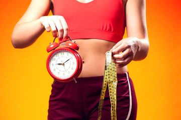 Woman in sportswear holding alarm clock and meter. People, fitness and healthcare concept