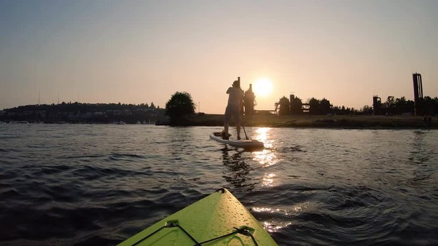 Kayak POV of Paddle Boarder Rowing into Sunset in Seattle Washington