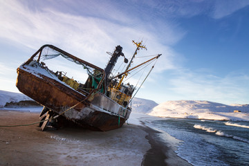 A fishing boat lying on its side, washed up by a storm on the shore of the Barents sea, the Kola...