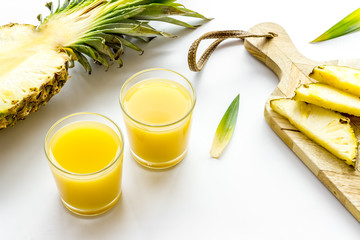 Pineapple juice in glass near sliced fruit on white background