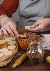 Cook's hands sculpting dumplings from rolled dough discs and pieces of minced meat