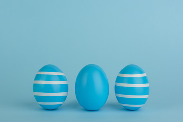  Three Easter decorated blue eggs. Striped blue eggs in a row on a blue background. White strips. Copy space. Blue monochrome.