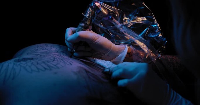 Close up of a tattoo artist making a tattoo with black ink on a person's back