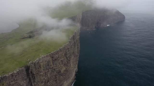Aerial flight above tall steep Faroe Islands sea cliffs, drone panoramic