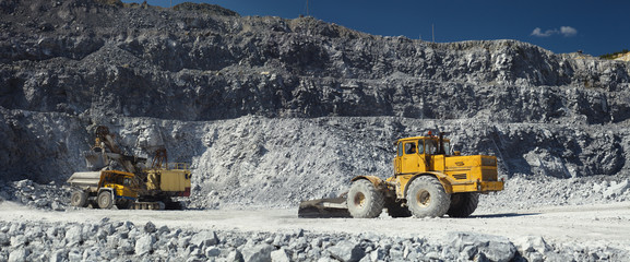 Mining excavator, heavy mining dump truck and tractor with a scraper in a quarry for the extraction of limestone. Panorama.