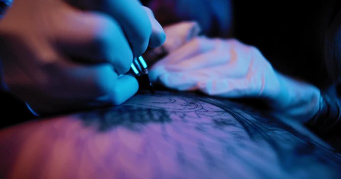 Tattoo artist making a tattoo on a person's back using blue paint. BMPCC 4K