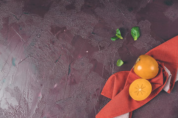 Healthy food background with persimmon and doucette (lambs-lettuce, cornsalad, field salad) with napkin on a red background, top view flat lay.