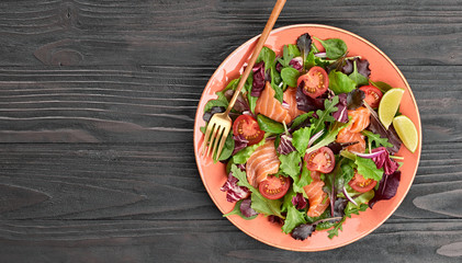 Salmon salad with cherry tomatoes, spinach, radicio, lollo on dish. Healthy seafood, salmon fish, creative diet concept. Tasty salmon and mixed leaves salad on dark wood, top view