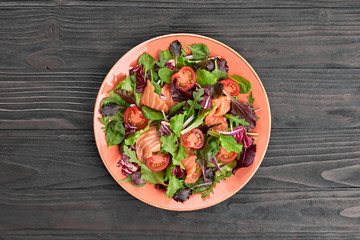 Salmon salad with cherry tomatoes, spinach, radicio, lollo on dish. Healthy seafood, salmon fish, creative diet concept. Tasty salmon and mixed leaves salad on dark wood, top view