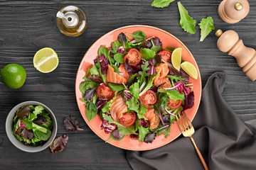 Salmon salad, cherry tomatoes, spinach, radicio, lollo. Home made vegetarian salmon salad. Seafood tasty concept. Mix leaves greens with salmon fish in plate on dark wood background.