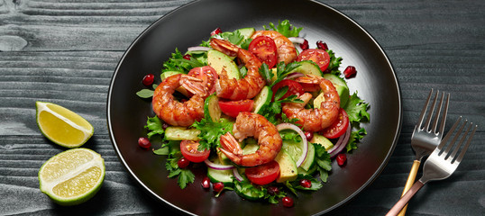 Shrimps salad, avocado, lettuce, cherry tomatoes. Home made vegetarian shrimp salad. Seafood concept. Tasty veg mixed leaves, grilled prawn shrimps in plate on black wood background.