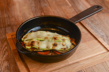 Backed eggplant with mozzarella cheese, tomatoes and basil served in a pan over rustic wooden board in a restaurant.