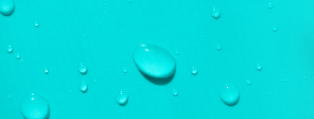 Close-up water drops on turquoise colored background, top view. Banner format backdrop