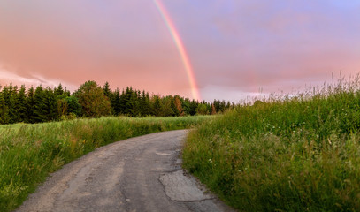 Rainbow over the summer field and road after the evening storm, sunset in countryside with...