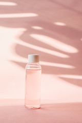 Plastic bottle with pink rose water on a pastel background with tropical shadow of a palm leaf. Transparent toner and toner to moisturize and cleanse the skin. Micellar water or cleansing foam