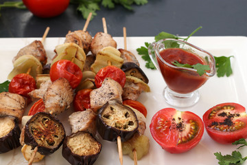 Shish kebab from turkey with vegetables: zucchini, eggplant, onion, tomato and pepper located on a white plate with sauce and tomatoes